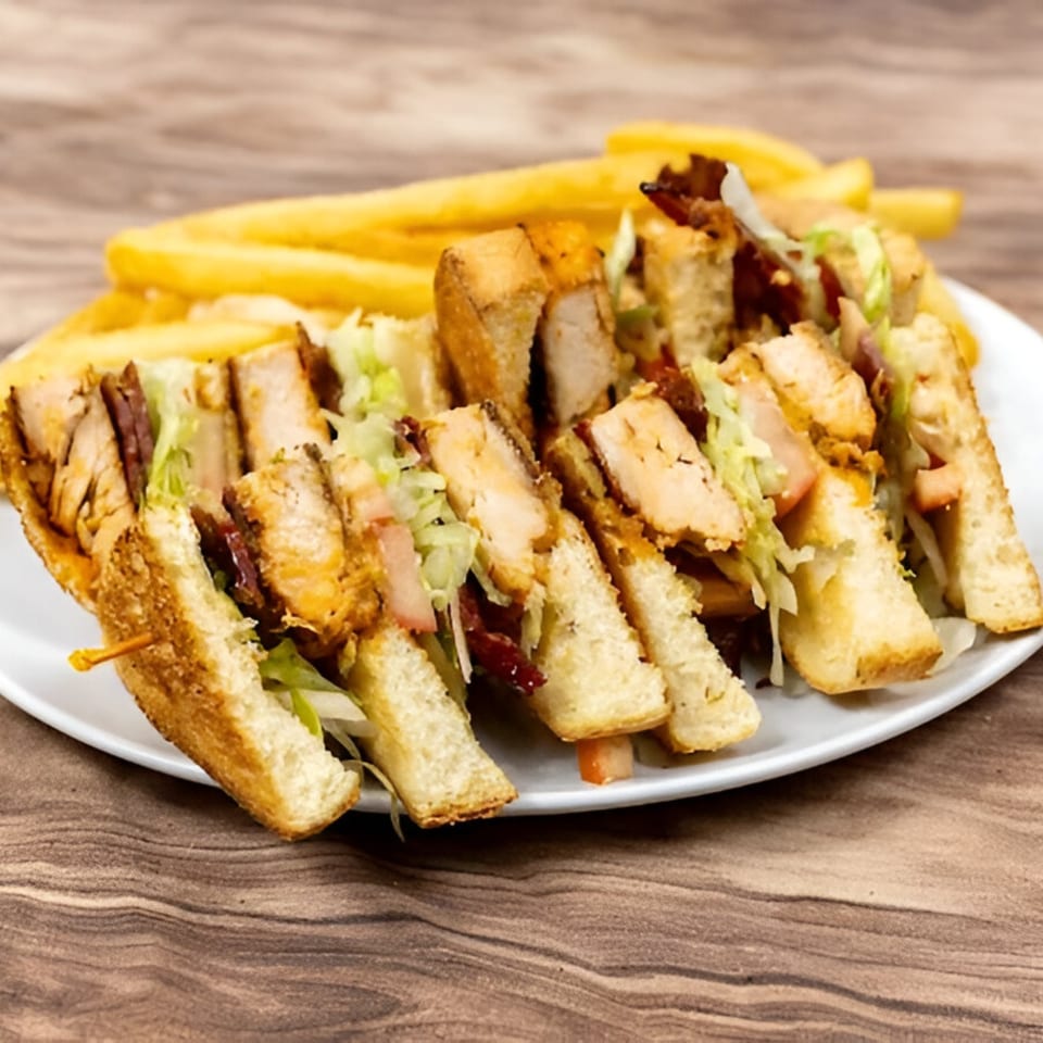 Chicken club sandwich with bacon, lettuce, and fries on a white plate.