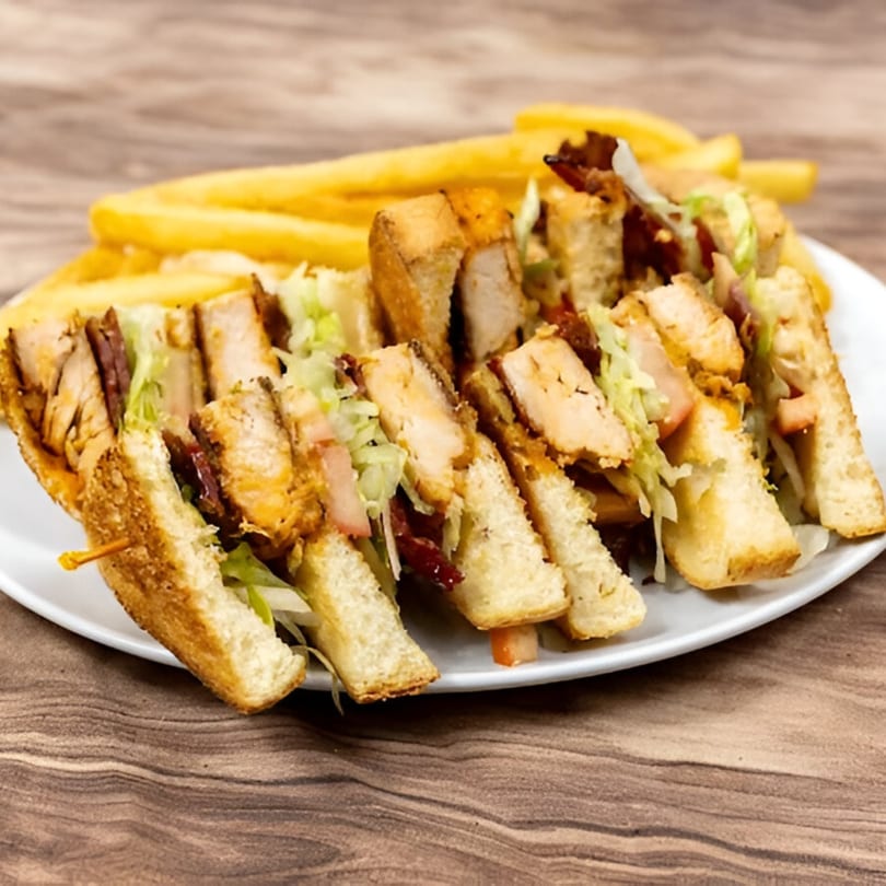 Chicken club sandwich with bacon, lettuce, and fries on a white plate.