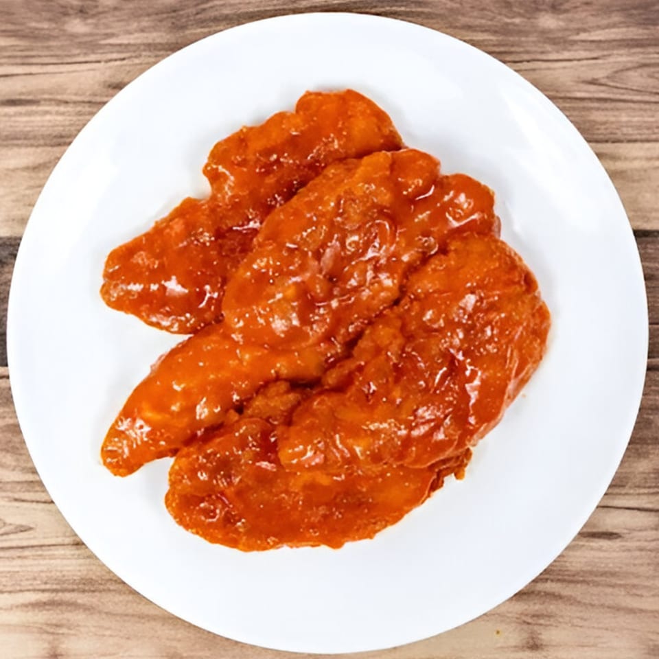 A white plate holds several pieces of Bravo Pizza's boneless wings coated in a glossy orange sauce.