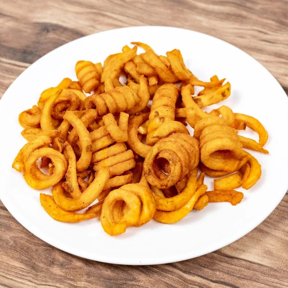 A white plate filled with golden-brown curly fries, seasoned with spices, on a wooden table.