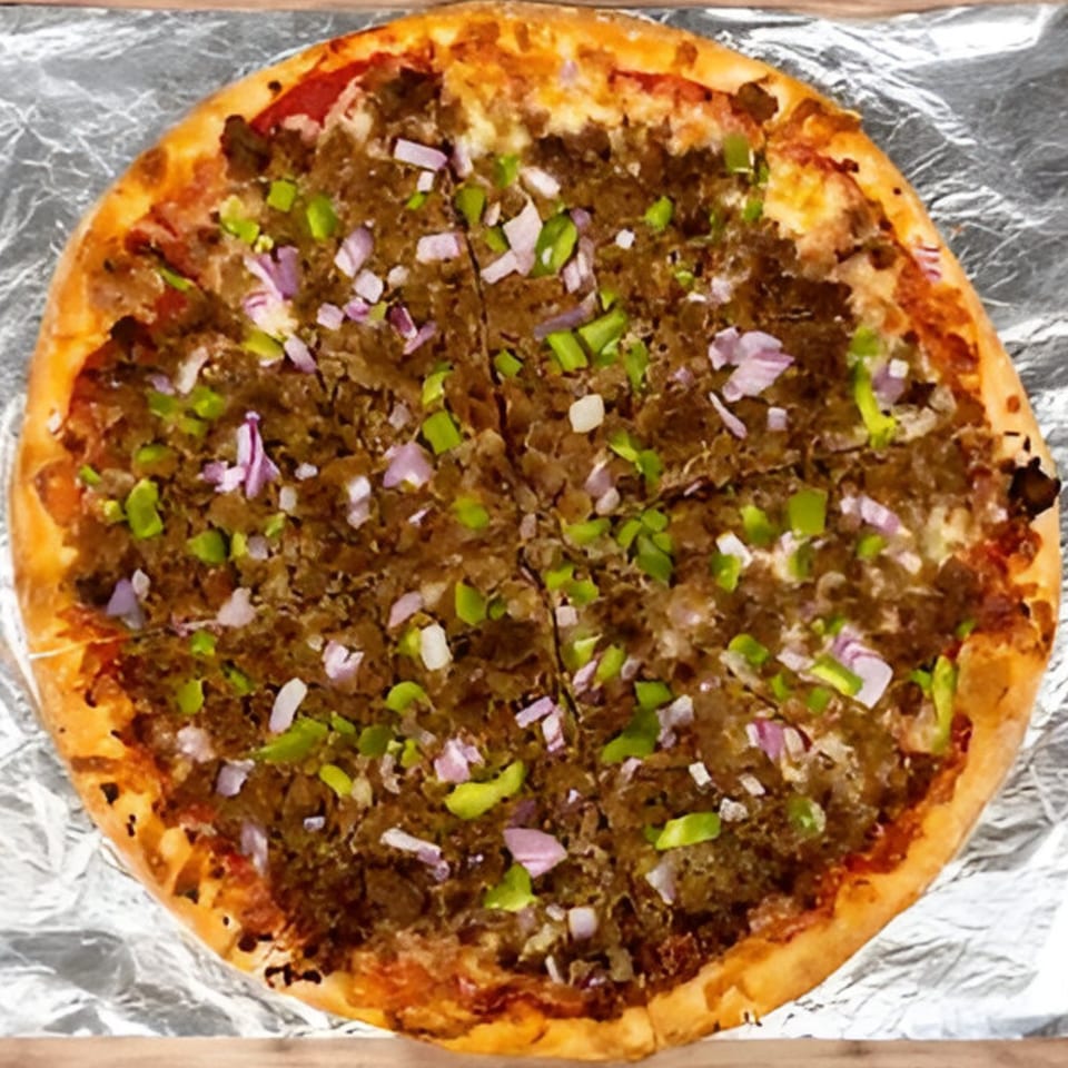 A Bravo Pizza with ground meat, green peppers, and red onions, sliced on aluminum foil.