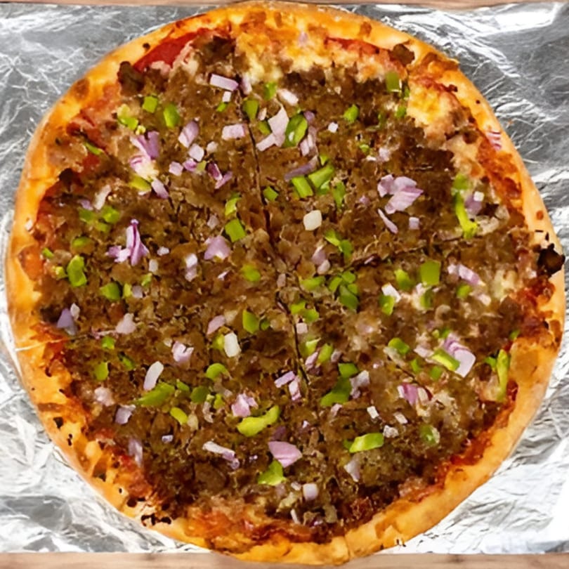 A Bravo Pizza with ground meat, green peppers, and red onions, sliced on aluminum foil.