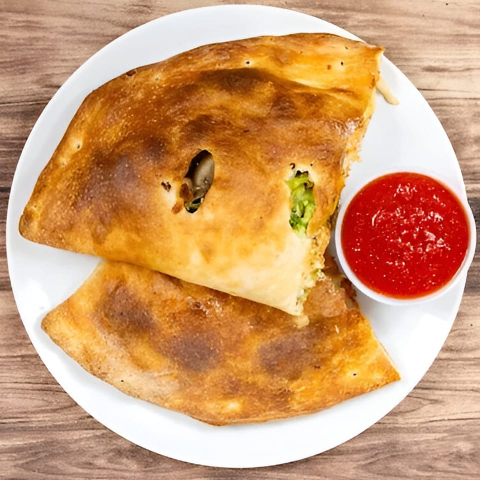 Two golden-brown calzones with visible green and mushroom fillings, served with a side of red marinara sauce.