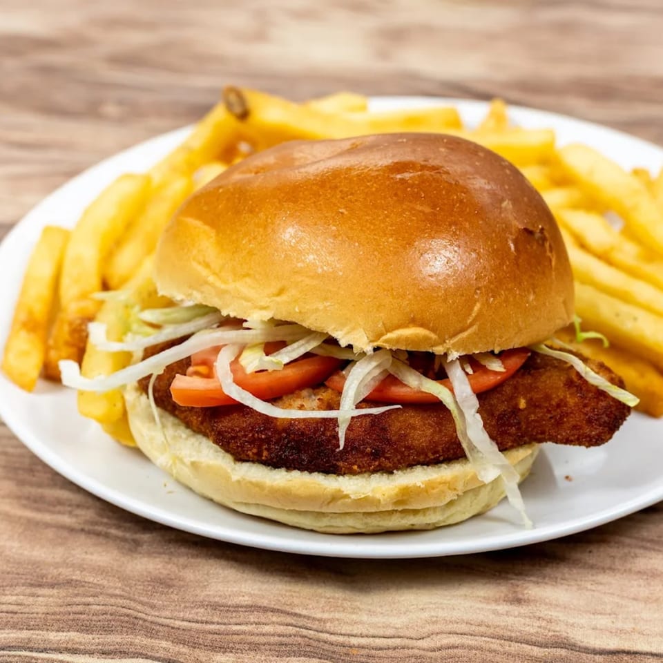 Crispy chicken sandwich with lettuce, tomato, and a side of golden french fries on a white plate.