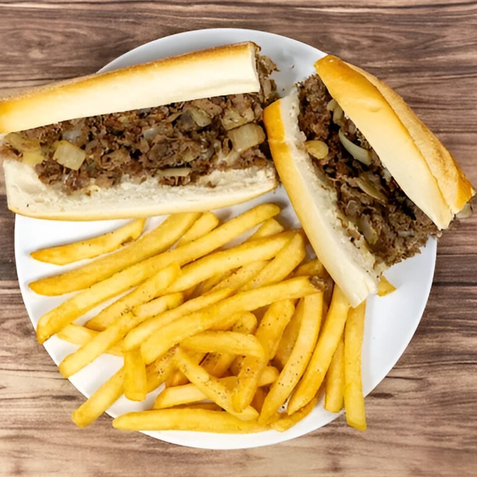 A Bravo Pizza cheesesteak sandwich, cut in half, served with a side of golden french fries.